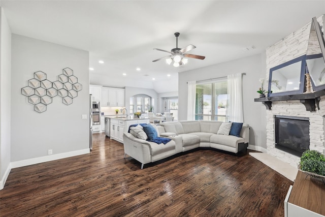 living room featuring a stone fireplace, dark wood finished floors, ceiling fan, and baseboards