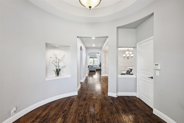 hallway with an inviting chandelier, arched walkways, baseboards, and wood finished floors