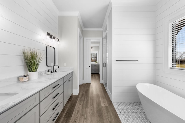 full bathroom featuring crown molding, double vanity, wood finished floors, a soaking tub, and a sink