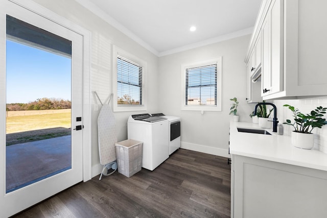 clothes washing area featuring dark wood-type flooring, independent washer and dryer, ornamental molding, a sink, and baseboards