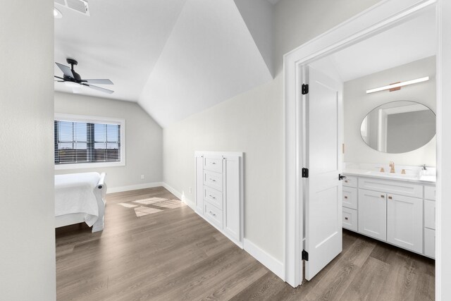 unfurnished bedroom featuring wood finished floors, baseboards, visible vents, a sink, and vaulted ceiling