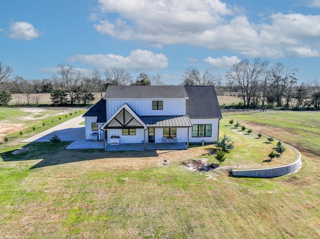 view of front of property featuring board and batten siding, a front lawn, a patio, metal roof, and a standing seam roof