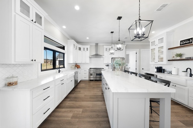 kitchen featuring a sink, a chandelier, appliances with stainless steel finishes, and wall chimney exhaust hood
