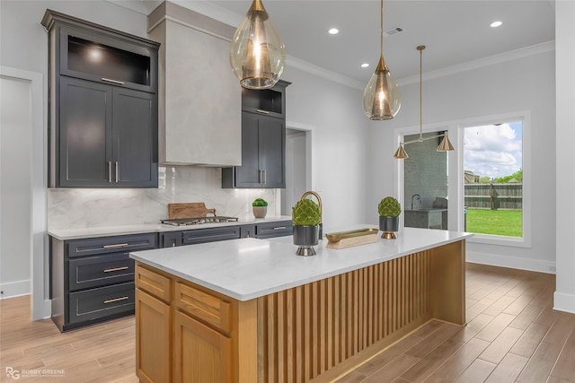 kitchen with crown molding, decorative backsplash, stainless steel gas stovetop, a kitchen island, and light wood finished floors