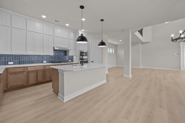 2012 Tolleson Dr, Fort Worth, TX 76008 - kitchen with stainless steel microwave, backsplash, light wood-style floors, light countertops, and an island with sink