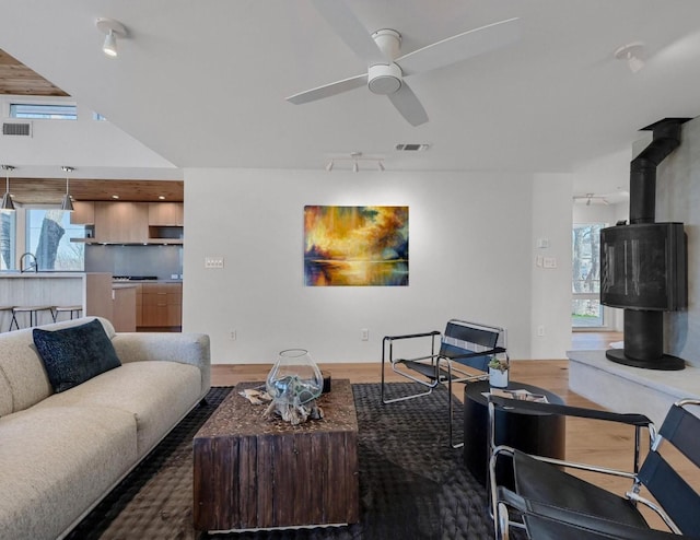 living area with visible vents, wood finished floors, a wood stove, and a ceiling fan