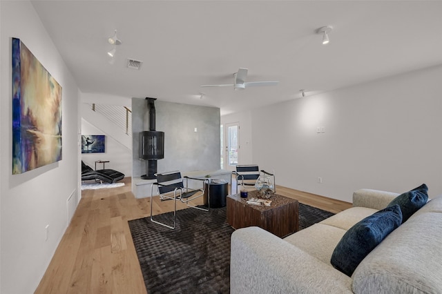 living area with ceiling fan, visible vents, wood finished floors, and a wood stove