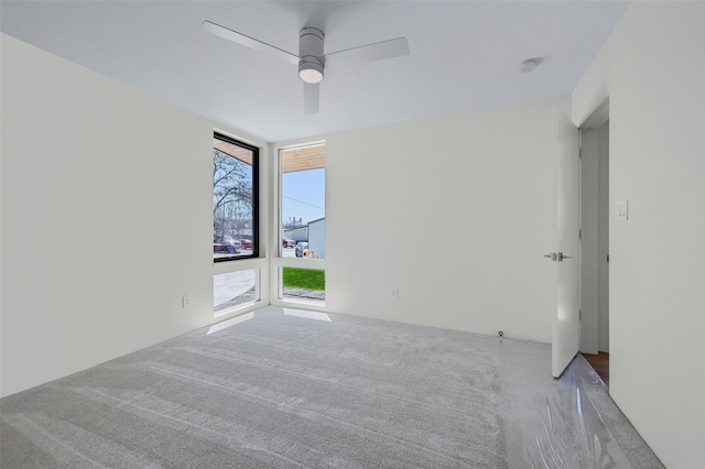 carpeted spare room with expansive windows and a ceiling fan