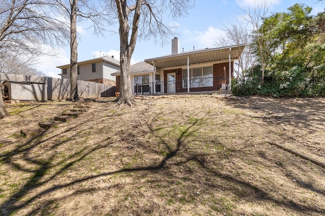 rear view of house featuring brick siding, a chimney, and fence