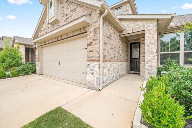 doorway to property with an attached garage, driveway, and stone siding