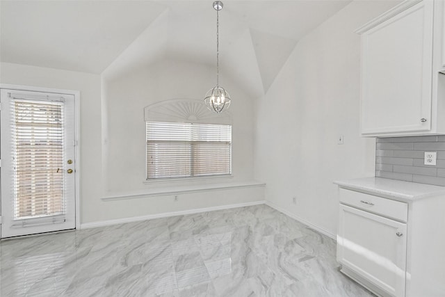 unfurnished dining area featuring a chandelier, lofted ceiling, light marble finish floors, and baseboards
