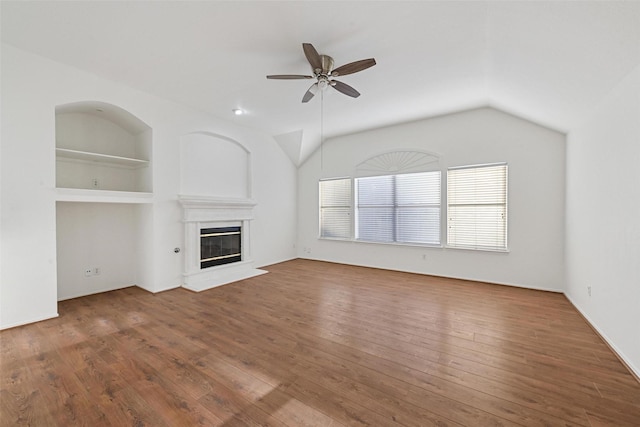 unfurnished living room with ceiling fan, a glass covered fireplace, wood finished floors, built in features, and vaulted ceiling