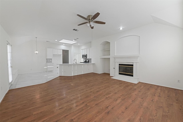 unfurnished living room with ceiling fan, a glass covered fireplace, wood finished floors, lofted ceiling, and built in features