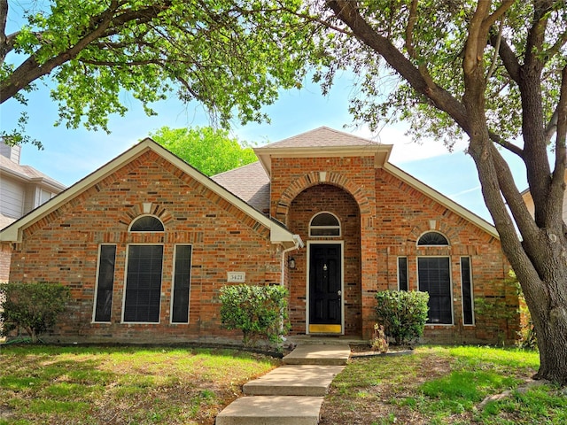traditional home with brick siding, roof with shingles, and a front lawn