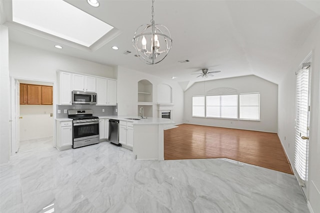 kitchen featuring stainless steel appliances, a sink, open floor plan, a peninsula, and vaulted ceiling