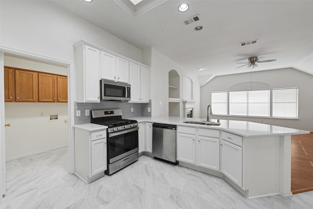 kitchen with a sink, stainless steel appliances, a peninsula, ceiling fan, and arched walkways
