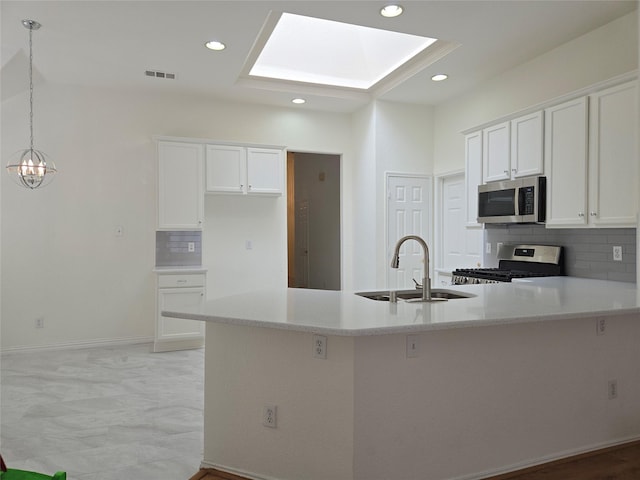 kitchen featuring stainless steel appliances, a sink, a peninsula, tasteful backsplash, and white cabinets