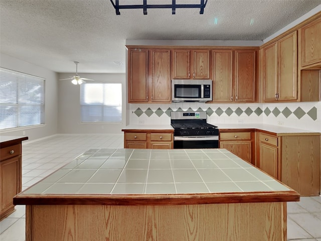 1114 Huntington Trl, Mansfield, TX 76063 - kitchen with tile countertops, ceiling fan, stainless steel appliances, backsplash, and a center island