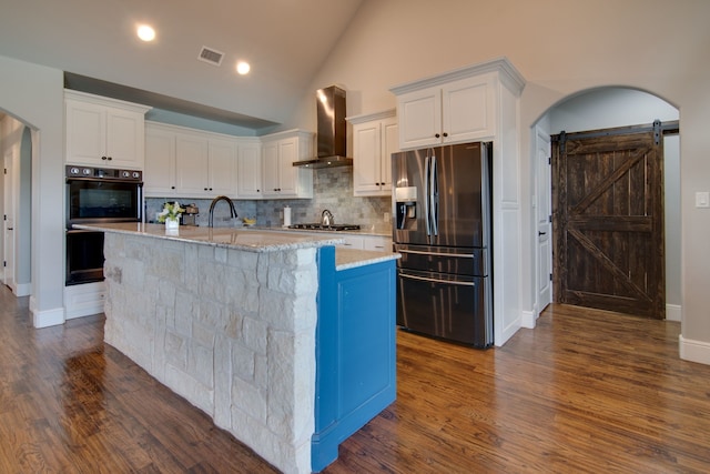 kitchen with wall chimney range hood, white cabinets, stainless steel appliances, decorative backsplash, and visible vents