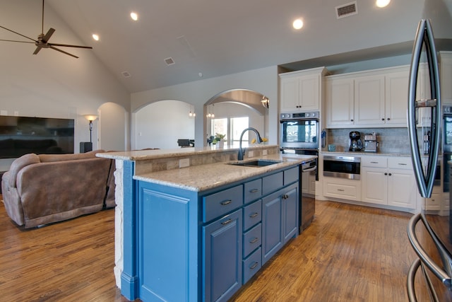 kitchen with stainless steel refrigerator, a sink, arched walkways, visible vents, and blue cabinets