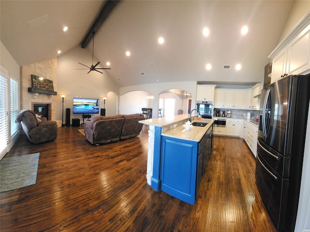kitchen with beam ceiling, a sink, fridge with ice dispenser, open floor plan, and oven