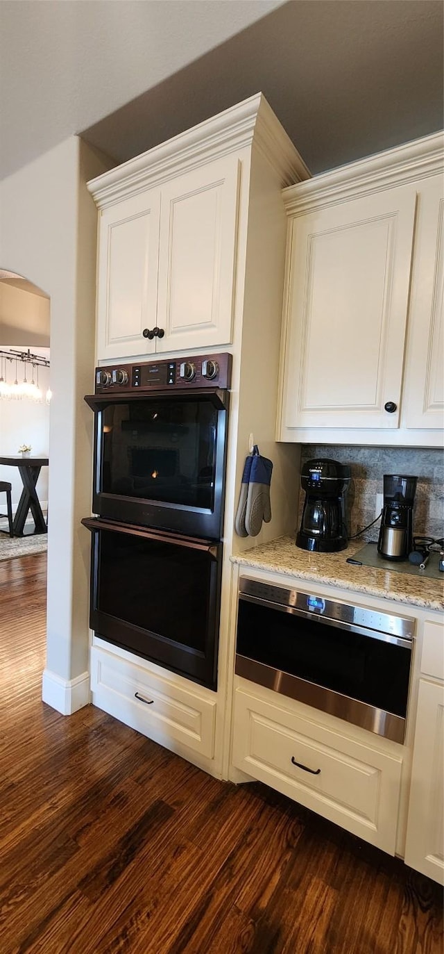 kitchen with white cabinets, dark wood-style flooring, light stone counters, dobule oven black, and tasteful backsplash