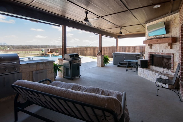 view of patio / terrace with ceiling fan, fence, grilling area, a fireplace, and exterior kitchen