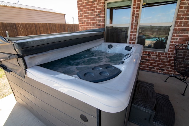 exterior details featuring a hot tub, brick siding, and fence