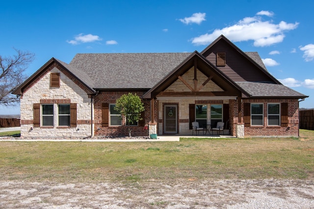 craftsman inspired home featuring roof with shingles, brick siding, a front lawn, a patio, and stone siding