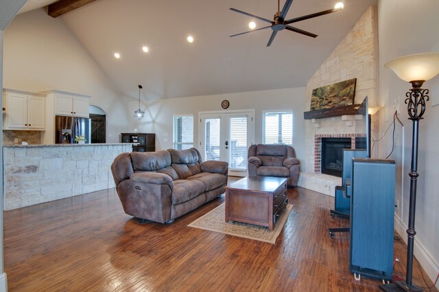 living area featuring dark wood-style flooring, ceiling fan, a fireplace, high vaulted ceiling, and beamed ceiling