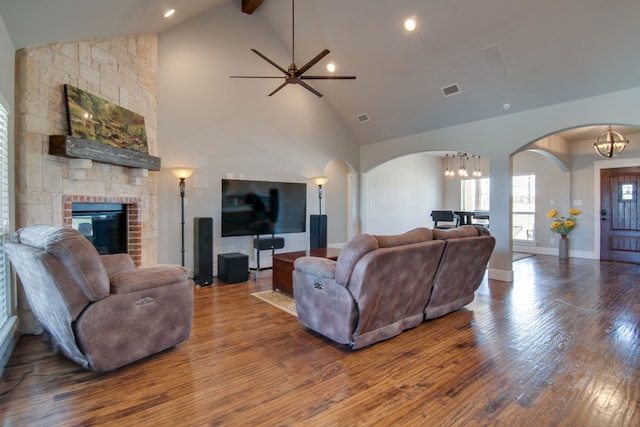 living area featuring visible vents, wood finished floors, a fireplace, high vaulted ceiling, and arched walkways