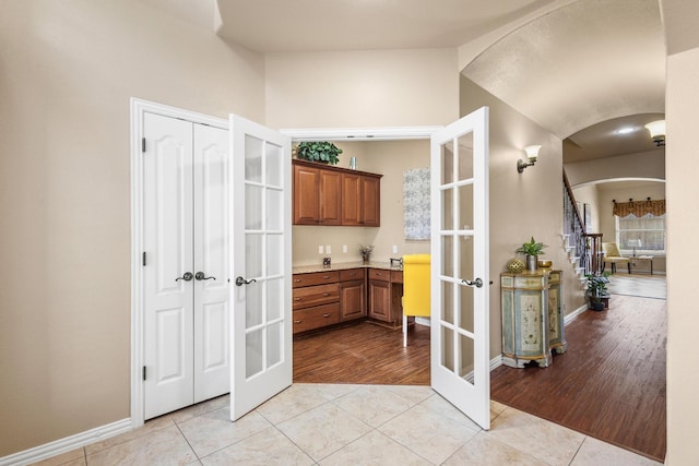 hallway featuring lofted ceiling, light tile patterned floors, baseboards, arched walkways, and french doors
