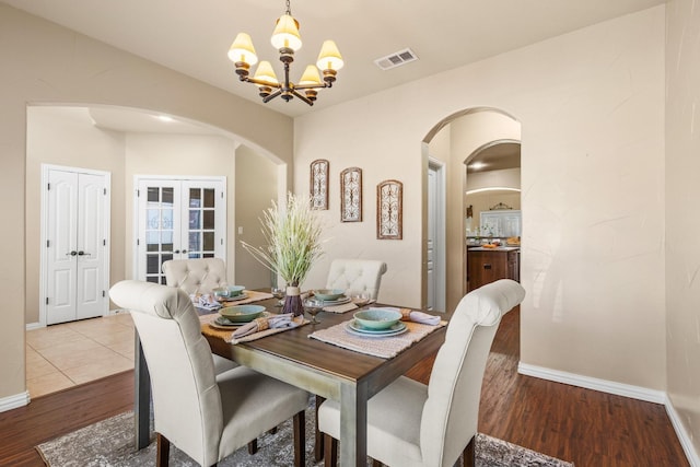 dining room with a chandelier, visible vents, arched walkways, and wood finished floors