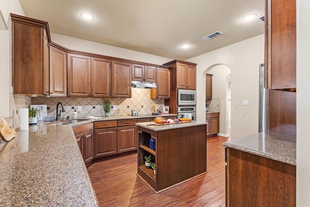 kitchen featuring a sink, under cabinet range hood, dark wood-type flooring, arched walkways, and appliances with stainless steel finishes