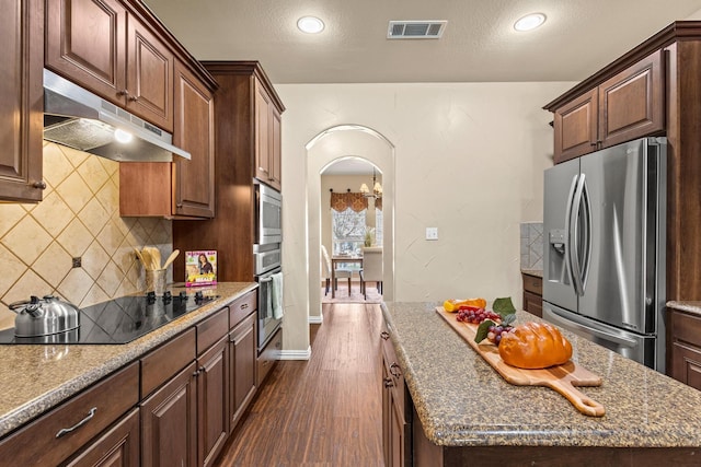 kitchen featuring dark wood-style flooring, under cabinet range hood, visible vents, arched walkways, and appliances with stainless steel finishes