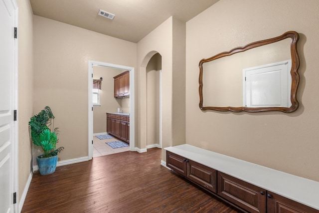 corridor with dark wood-style floors, visible vents, and baseboards
