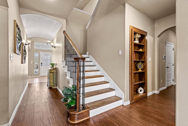 interior space with arched walkways, stairway, wood finished floors, and baseboards