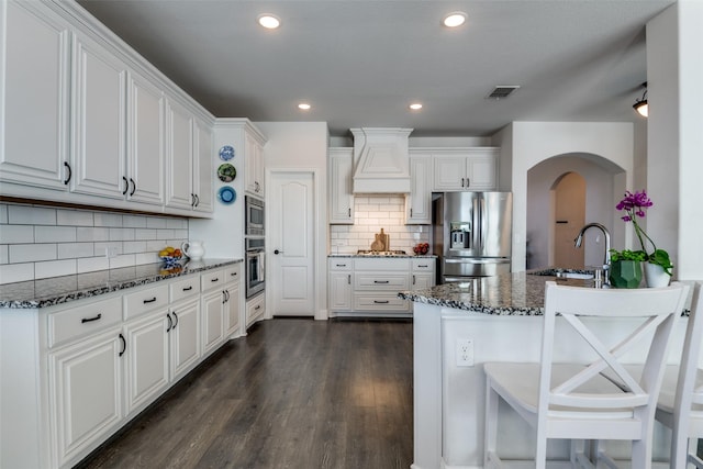 kitchen featuring stainless steel appliances, arched walkways, a sink, visible vents, and custom exhaust hood