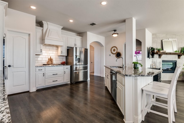 kitchen featuring stainless steel appliances, a sink, dark stone countertops, visible vents, and custom range hood