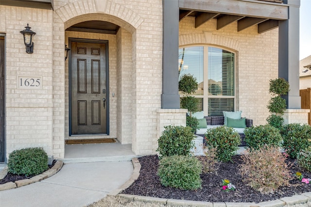 view of exterior entry featuring brick siding and covered porch
