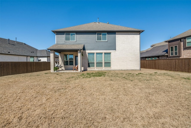 rear view of property featuring a patio area, a fenced backyard, brick siding, and a yard