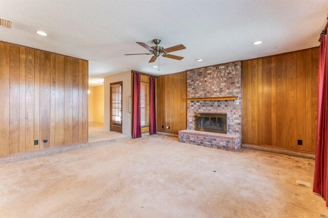 unfurnished living room featuring a ceiling fan, carpet floors, wood walls, a textured ceiling, and a brick fireplace