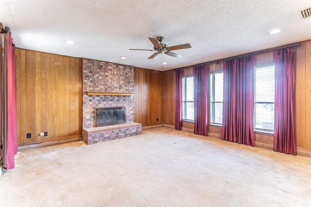 unfurnished living room with a brick fireplace, wooden walls, carpet, and ceiling fan