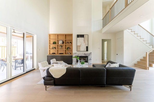 living room featuring a towering ceiling, wood finished floors, stairs, a fireplace, and baseboards