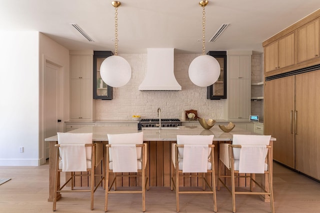 kitchen featuring premium range hood, backsplash, a breakfast bar area, paneled built in refrigerator, and a center island with sink