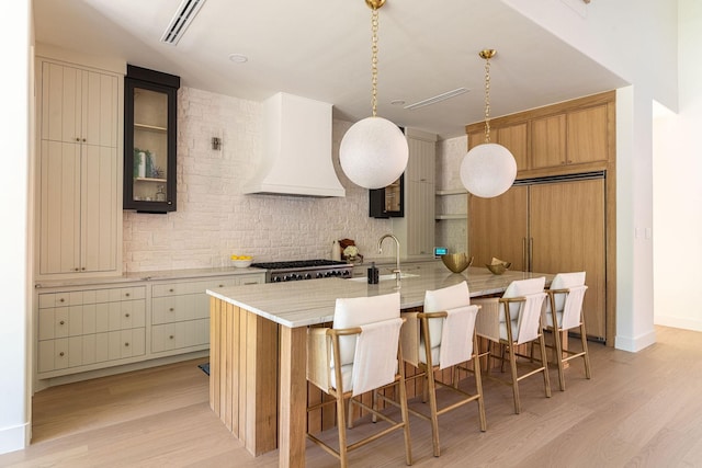 kitchen featuring custom range hood, light wood finished floors, tasteful backsplash, and a sink