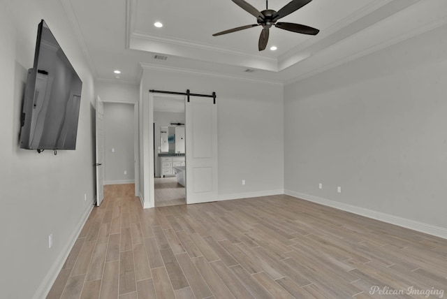 unfurnished bedroom with light wood-style floors, visible vents, a raised ceiling, and a barn door