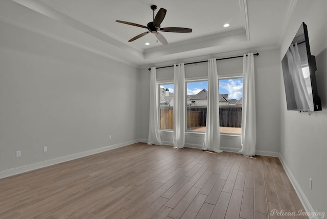 empty room with baseboards, a raised ceiling, ceiling fan, and light wood finished floors
