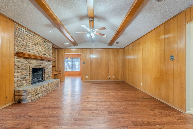 unfurnished living room with wooden walls, vaulted ceiling with beams, wood finished floors, and a textured ceiling