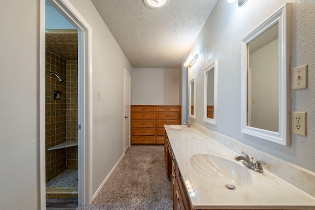 full bath featuring a textured ceiling, double vanity, a tile shower, and a sink